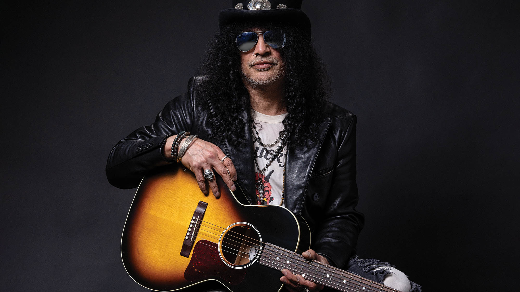 Slash wears a top hat and holds a GIbson J-45 acoustic guitar