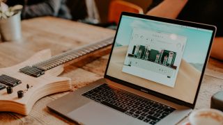 A laptop with a Neural DSP plugin running on a wooden table with a guitar in the background