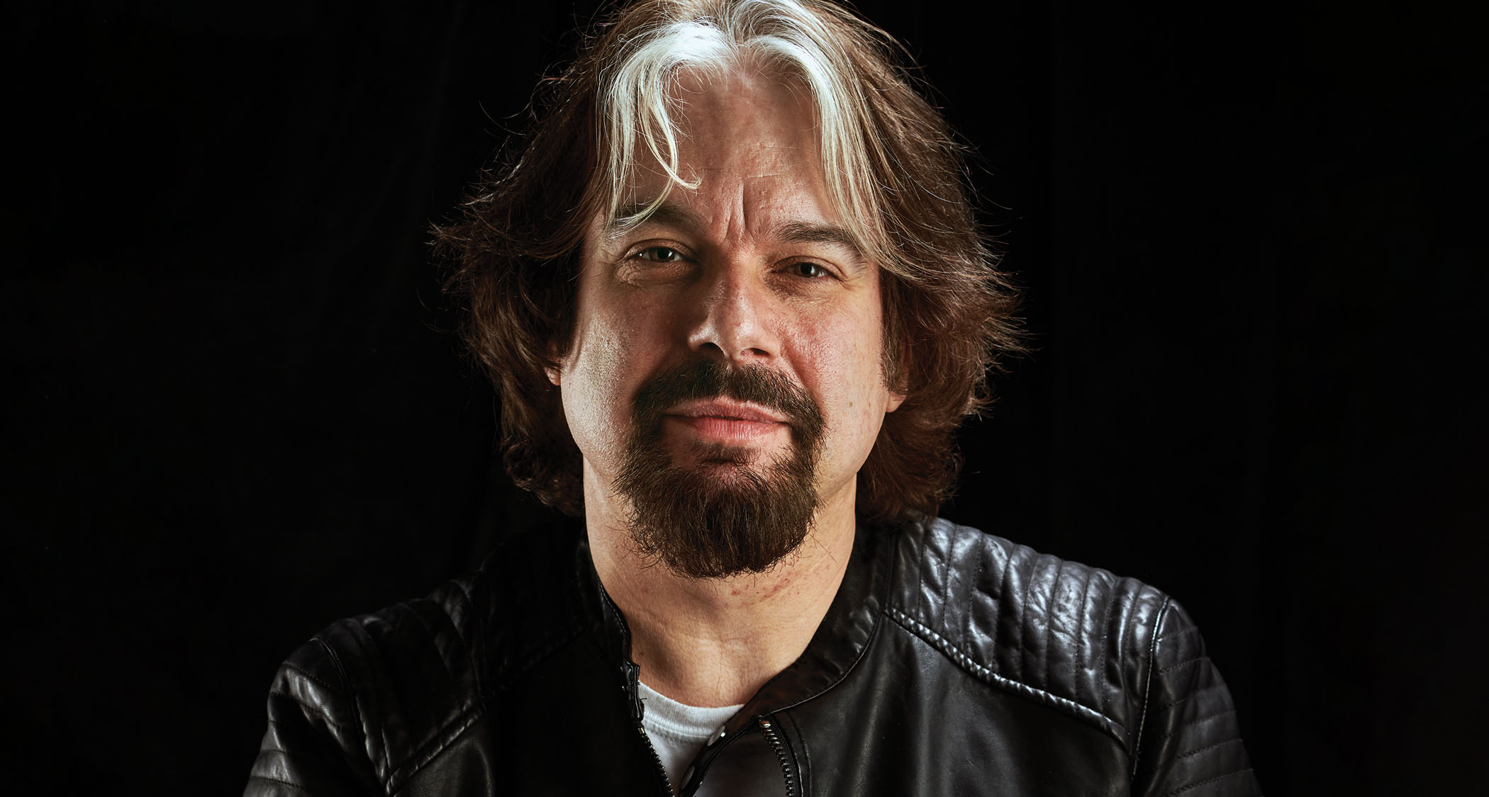 Dan Coggins, the man behind the iconic Lovetone pedals brand and regular collaborator of ThorpyFX, is pictured wearing a black leather jacket against a black background.