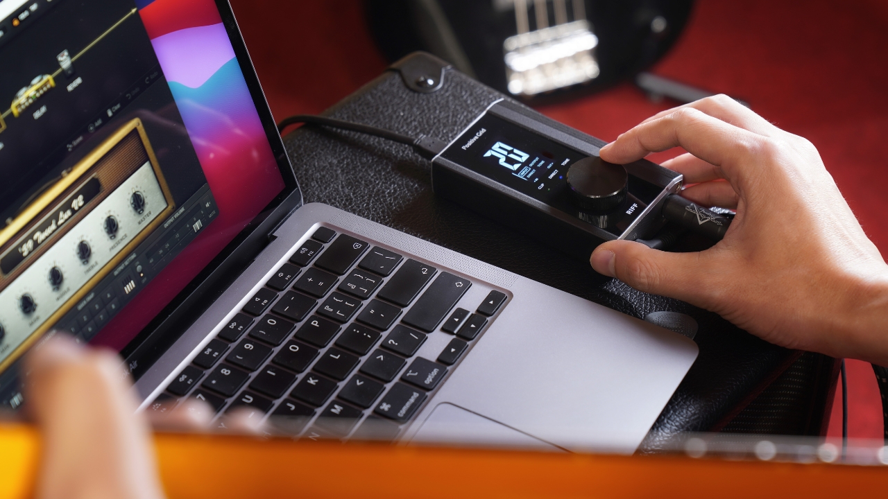 A man turns a knob on a Positive Grid Riff audio interface on top of a guitar amp next to a MacBook