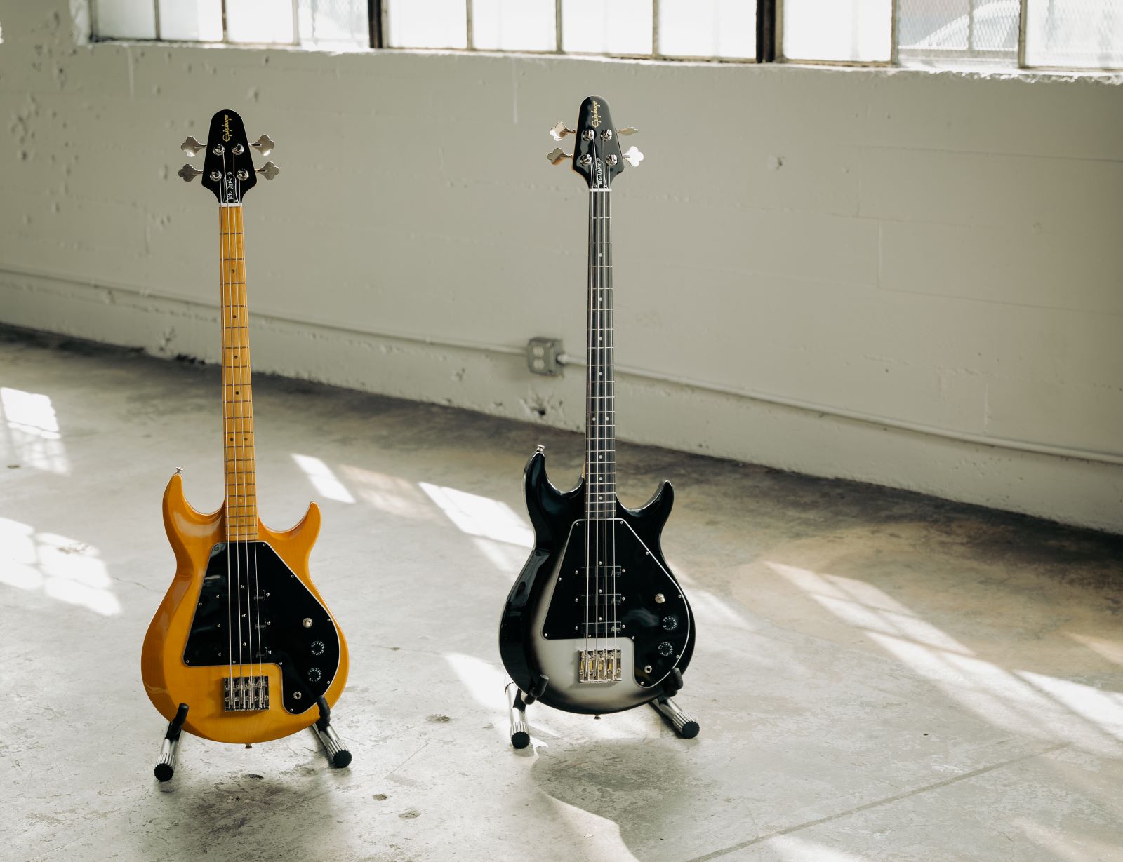 A photo showing the Mike Dirnt Epiphone Grabber G-3 Bass in natural (left) and Silverburst (right) finishes.