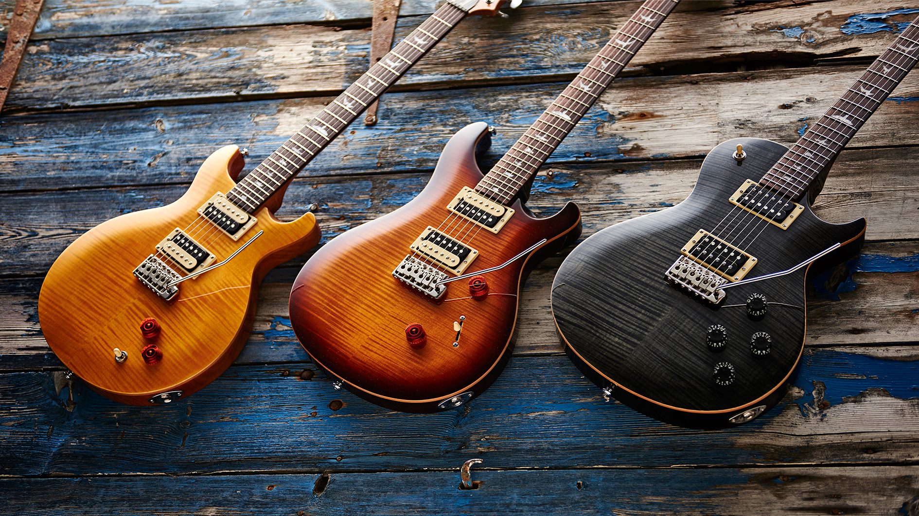 Three PRS guitars lying against a distressed wooden floor