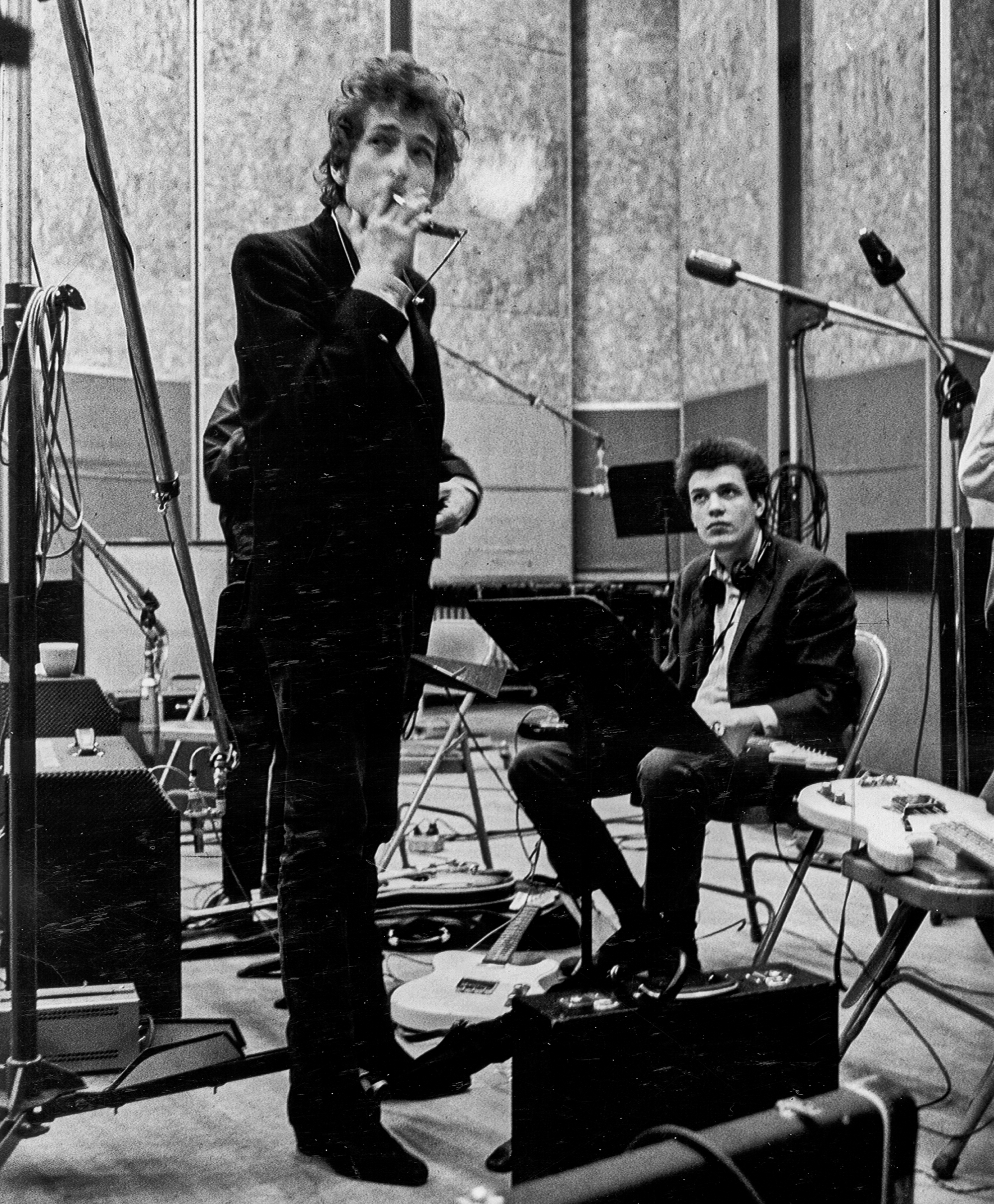 NEW YORK - SUMMER 1965: Bob Dylan (holding a cigarette) and guitarist Mike Bloomfield (seated) take a break during the recording of the album 'Highway 61 Revisited' surrounded by an assortment of microphones, amplifiers and guitars in Columbia's Studio A in the summer of 1965 in New York City, New York.
