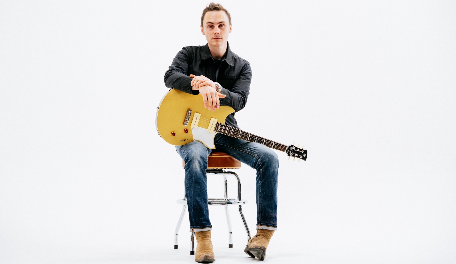 Chris Buck, seated in a chair against a white background, holds his new Yamaha RS02CB signature guitar