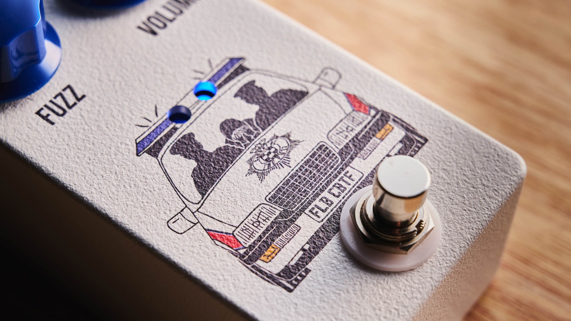 Funny Little Boxes Caught By The Fuzz: inspired by Supergrass, this two-knob fuzz has a white enclosure, blue dials, and a comic graphic of someone being apprehended in a police car.