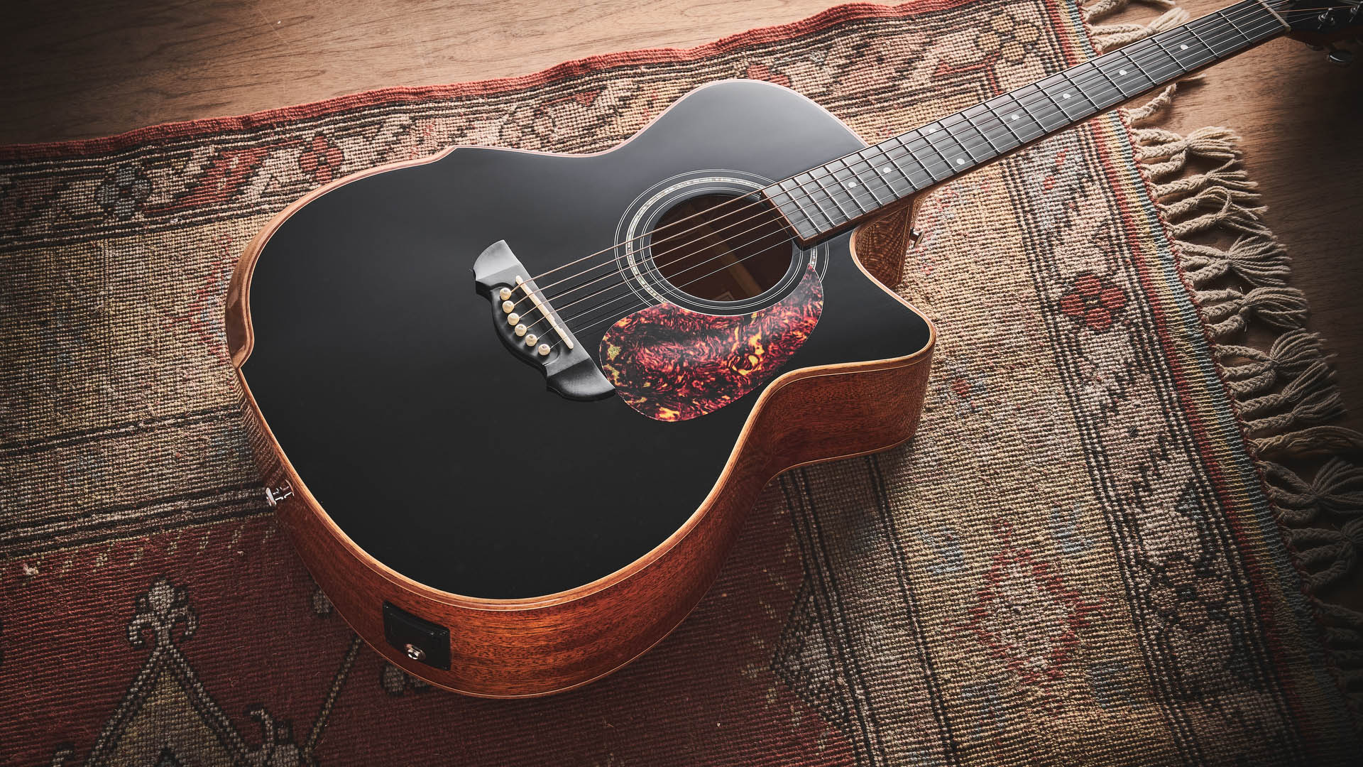Harley Benton CLG-650SM-CE Black: the handsome but affordable cutaway acoustic isd photographed against a patterned rug on a wooden floor.