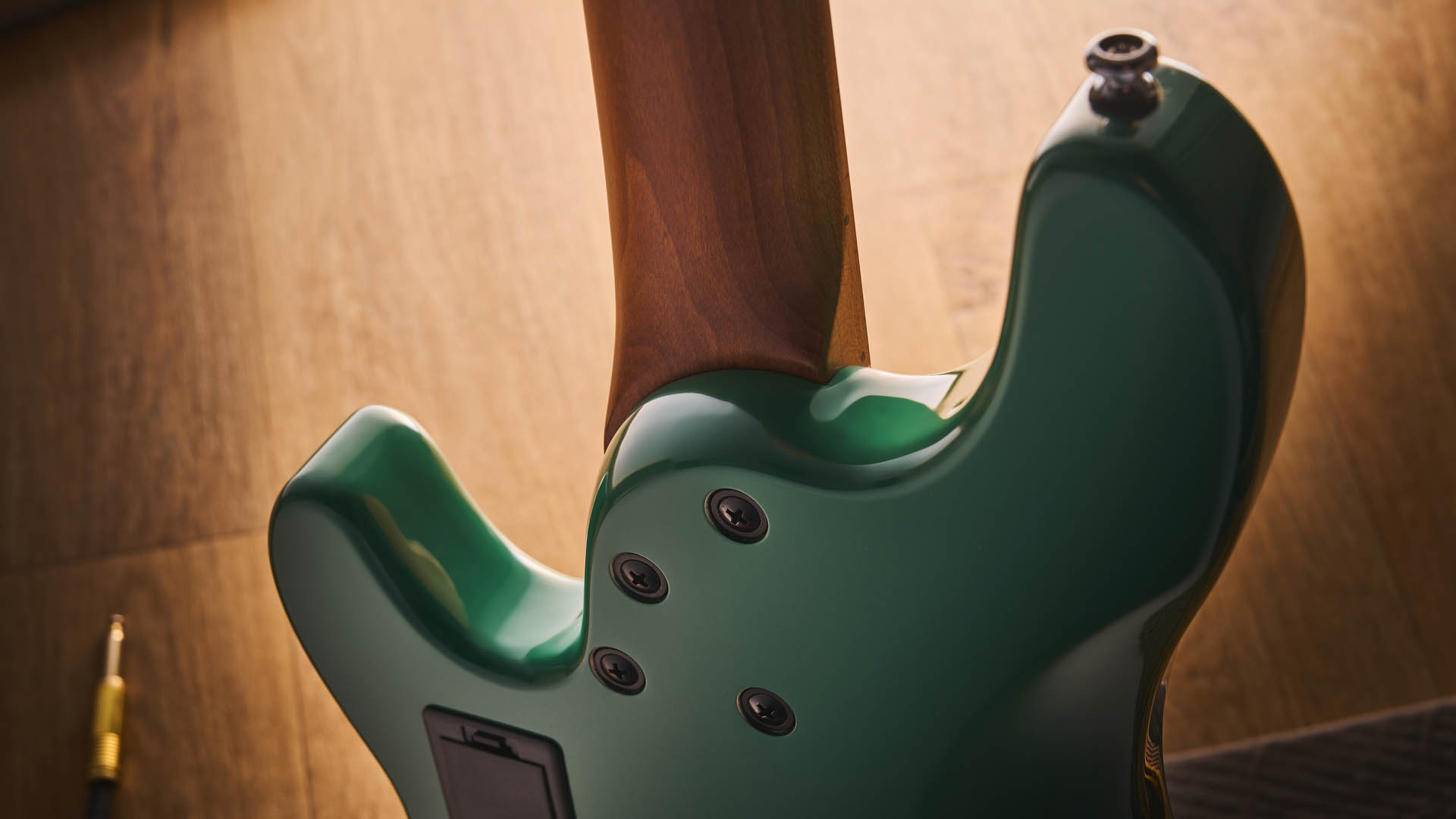 The Cort GB-Short Scale Bass finished in green, photographed against a light wooden floor and rug.