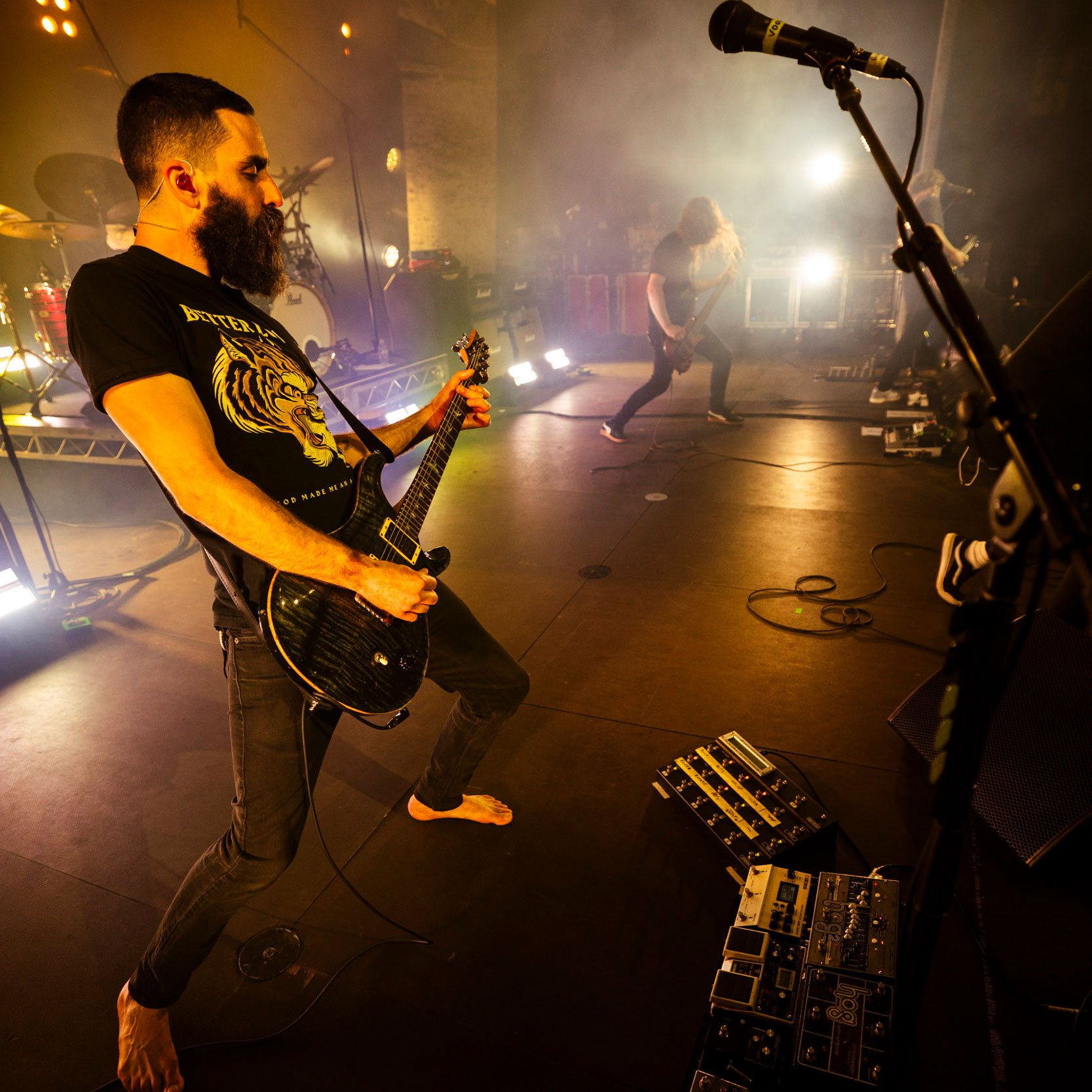 Karnivool guitarist Drew Goddard playing onstage, in bare feet, with his pedalboards and PRS guitar in shot
