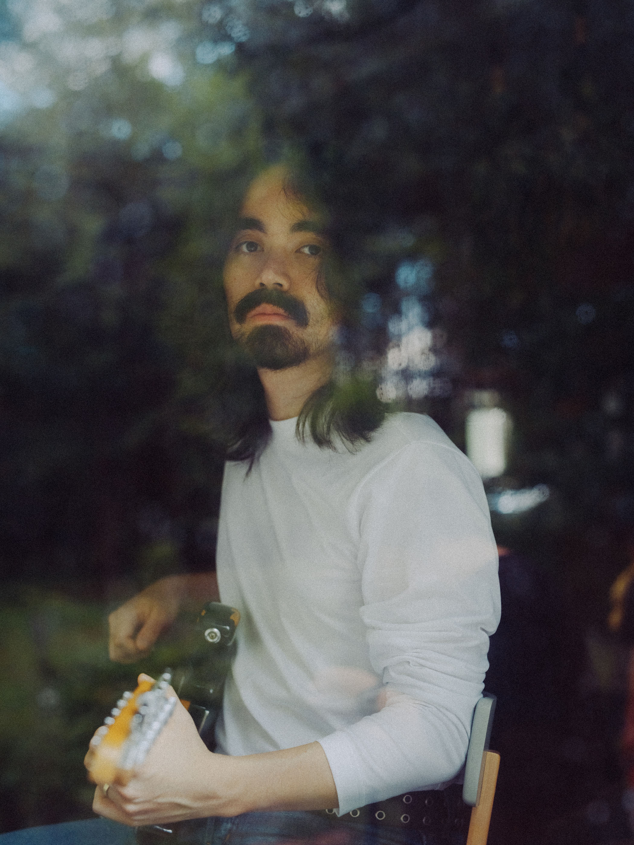 A side-on photo of Mateus Asato seated, playing guitar.