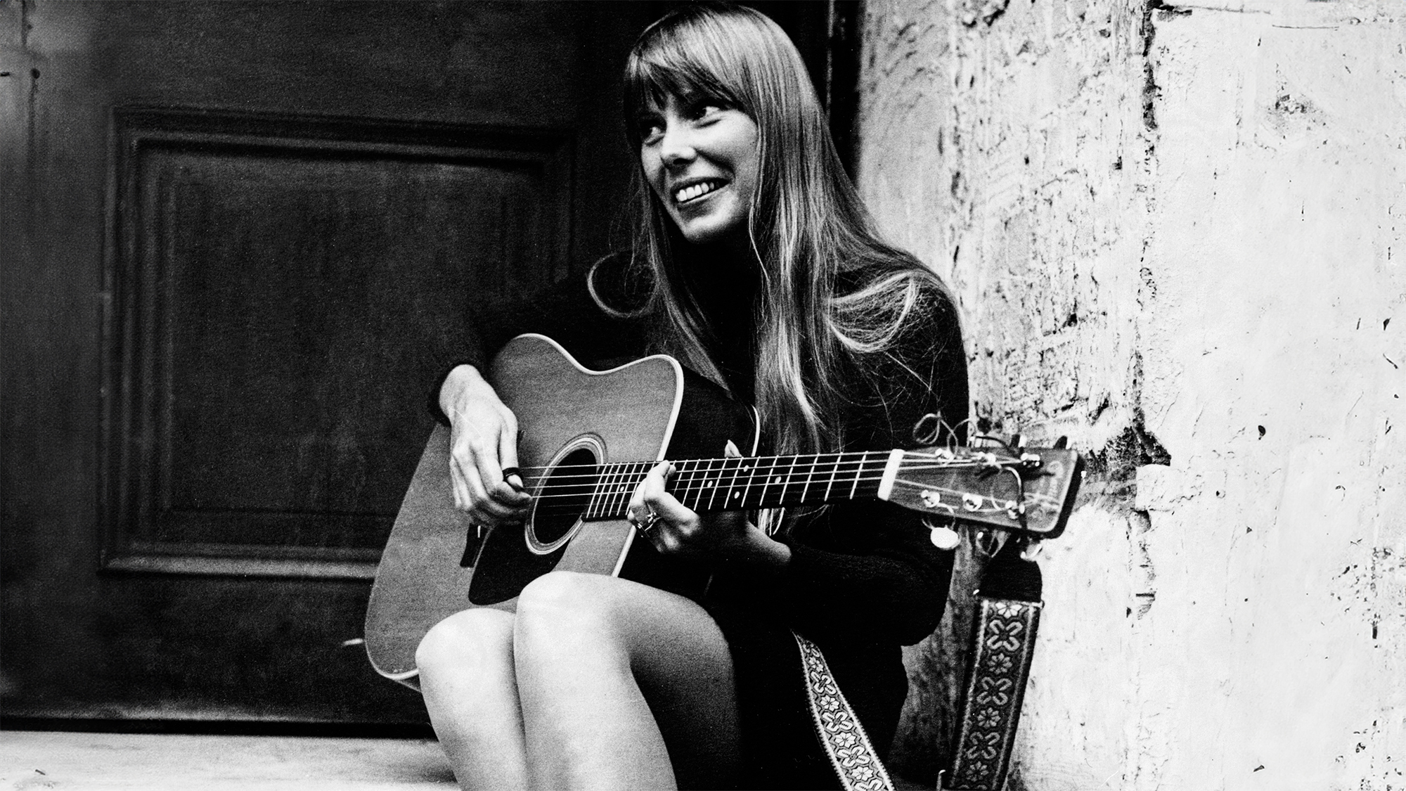(Original Caption) A singer called Joni. Joni Mitchell, Canadian singer-songwriter, United Kingdom, 1968. The guitar-pickin' gal is Joni Mitchell, a long blonde haired Canadian folk singer. Pictured last night outside the Revolution club, Joni is here (until 1st October) for radio, television and concert appearances. Apart from concert appearances, 25 year old Joni will be heard on "Top Gear" on Radio One and "The Monday Show" on BBC 1.