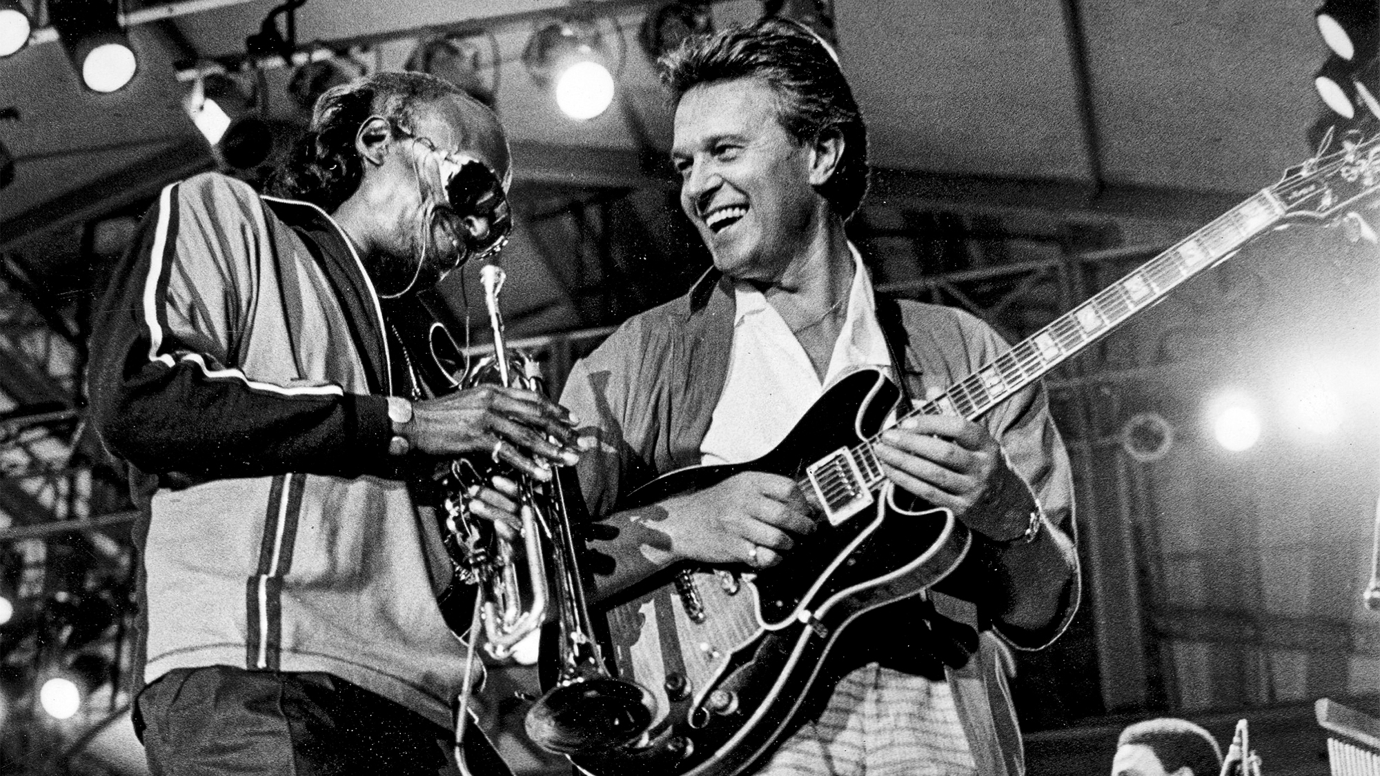 Miles Davis (1926-1991), American jazz composer and trumpeter, and John McLaughlin (born in 1942), English guitarist, during a concert, 1985.