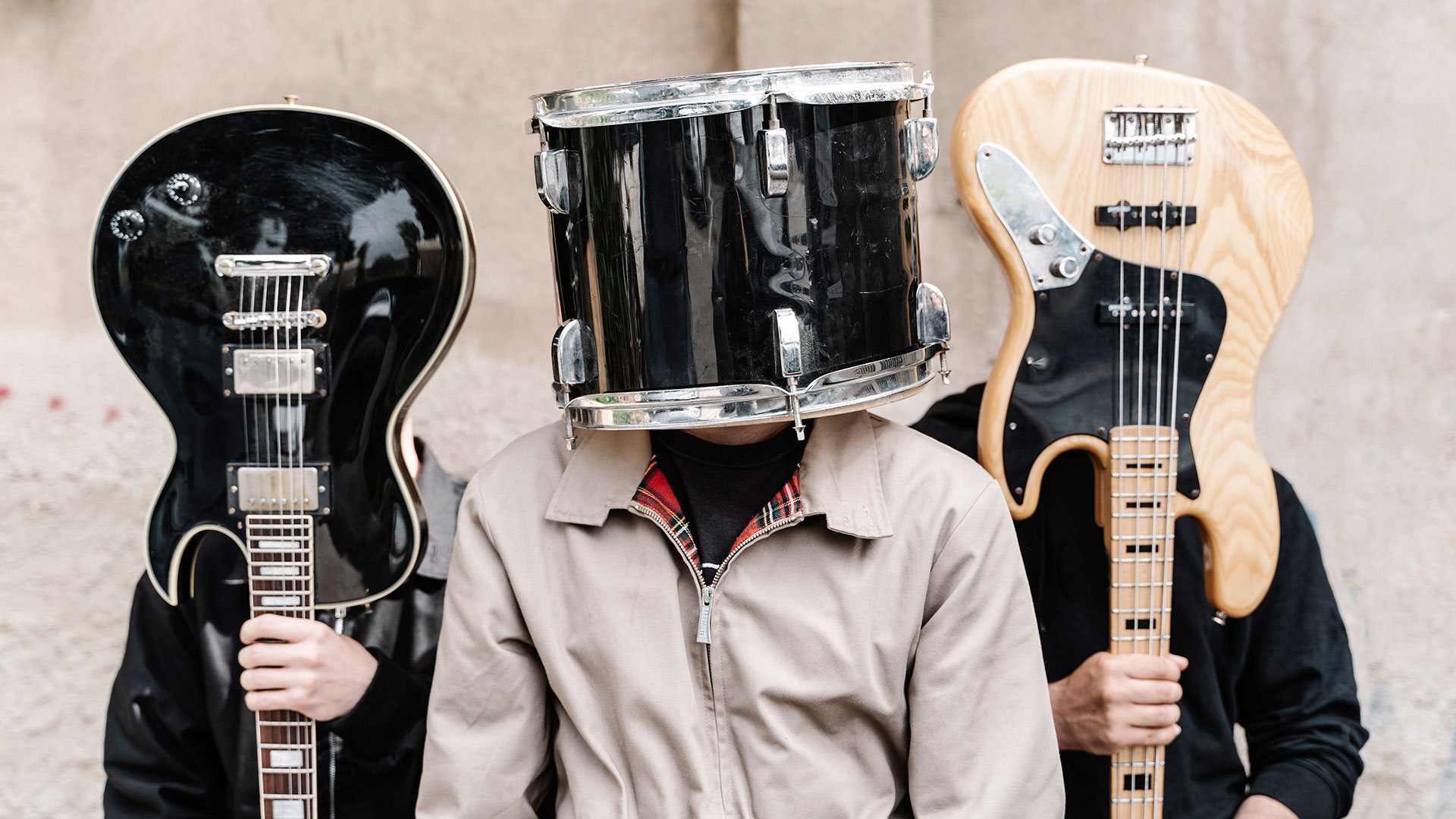 Three musicians, with faces obscured by their instruments &ndash;&nbsp;L-R guitarist, drummer and bassist