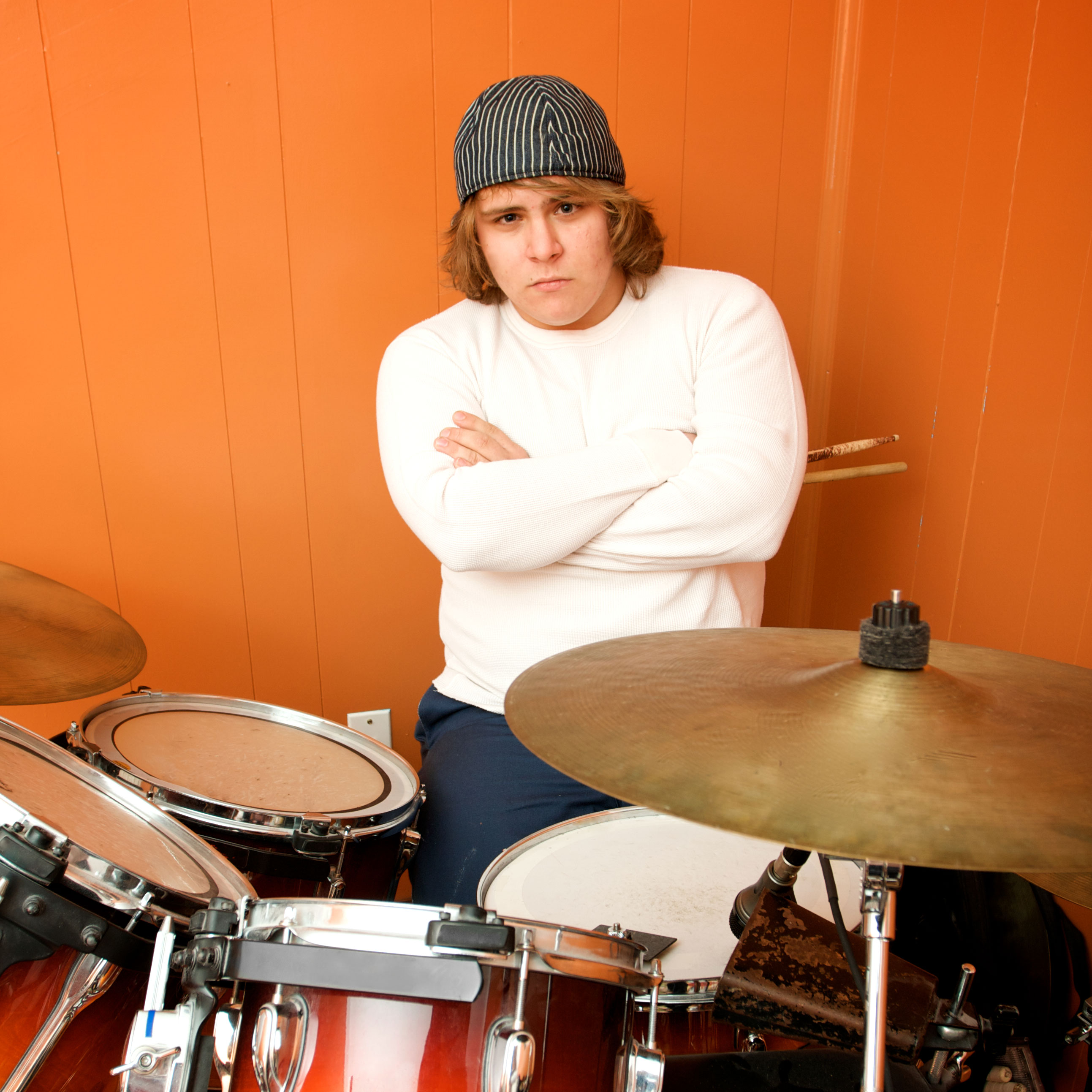 Grumpy drummer in a white shirt leans against an orange wall