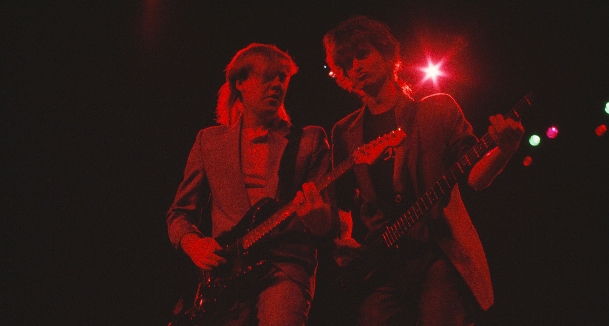 Alex Lifeson and Geddy Lee are bathed in red light as they perform with Rush in the 1985.
