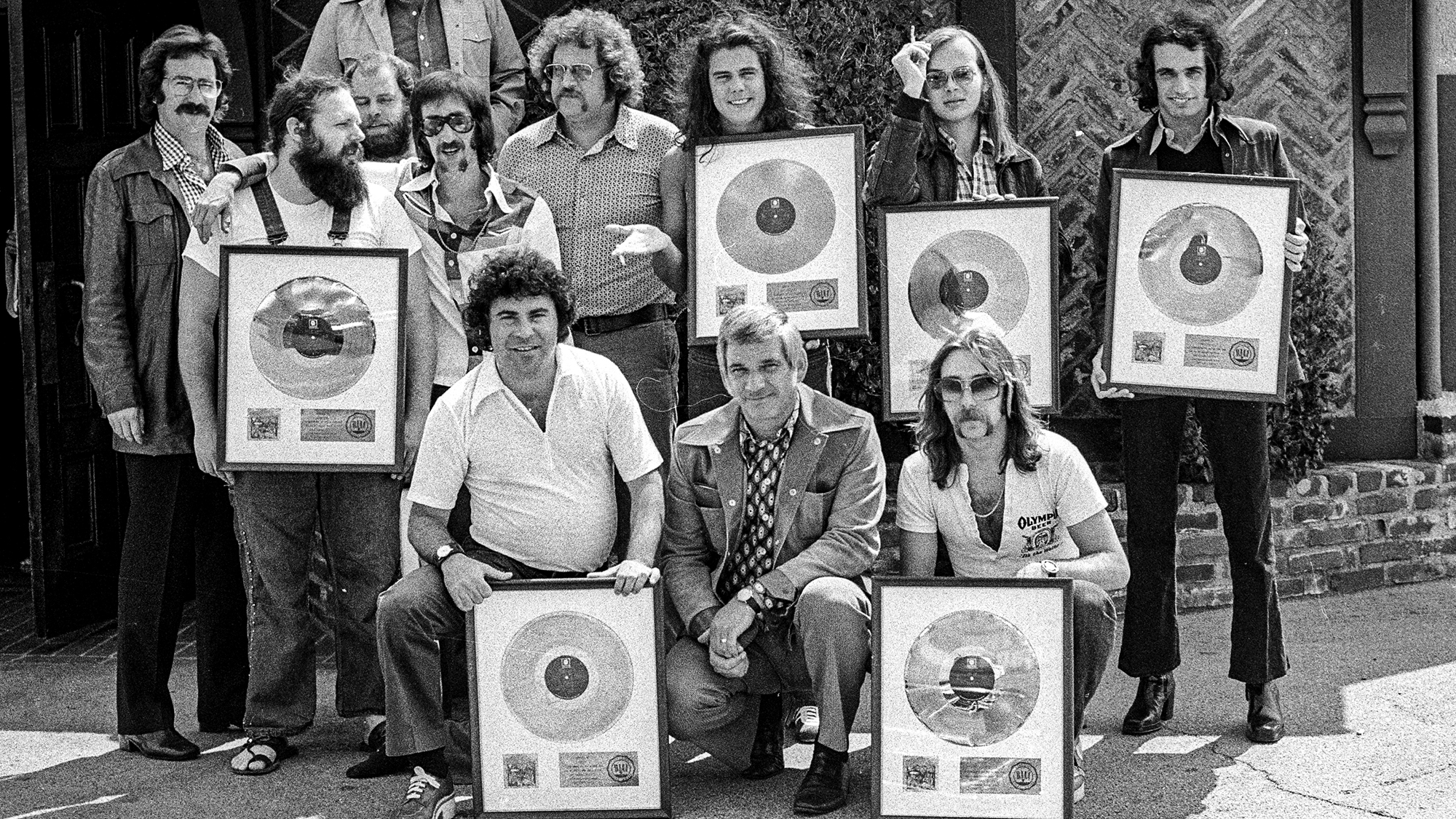 LOS ANGELES - 1973: Front Row L-R: (kneeling) Joel Cohn, Manager; Marv Helfer, Manager, Jeff Skunk Baxter, Second Row L-R: (standing) Howard Rose, booking agent; Denny Dias; Bob Gibson, Publicist; Gary Katz, Producer; Dennis Lavinthol, Sr. VP Promotions ABC Dunhill Records; Jim Hodder, Walter Becker, Donald Fagen, Top row (standing with arms outstretched) Jay Lasker, Presisdent ABC/Dunhill Records at the gold record presentation to rock band Steely Dan for the song "Can't Buy A Thrill" at ABC/Dunhill Records in 1973 in Los Angeles, California.