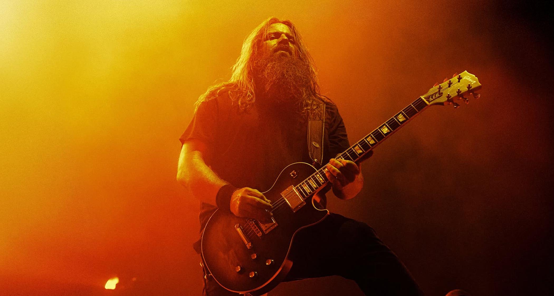 Lamb of God's Mark Morton performs live on a stage lit in yellow and orange. He plays his new Les Paul Modern Quilt