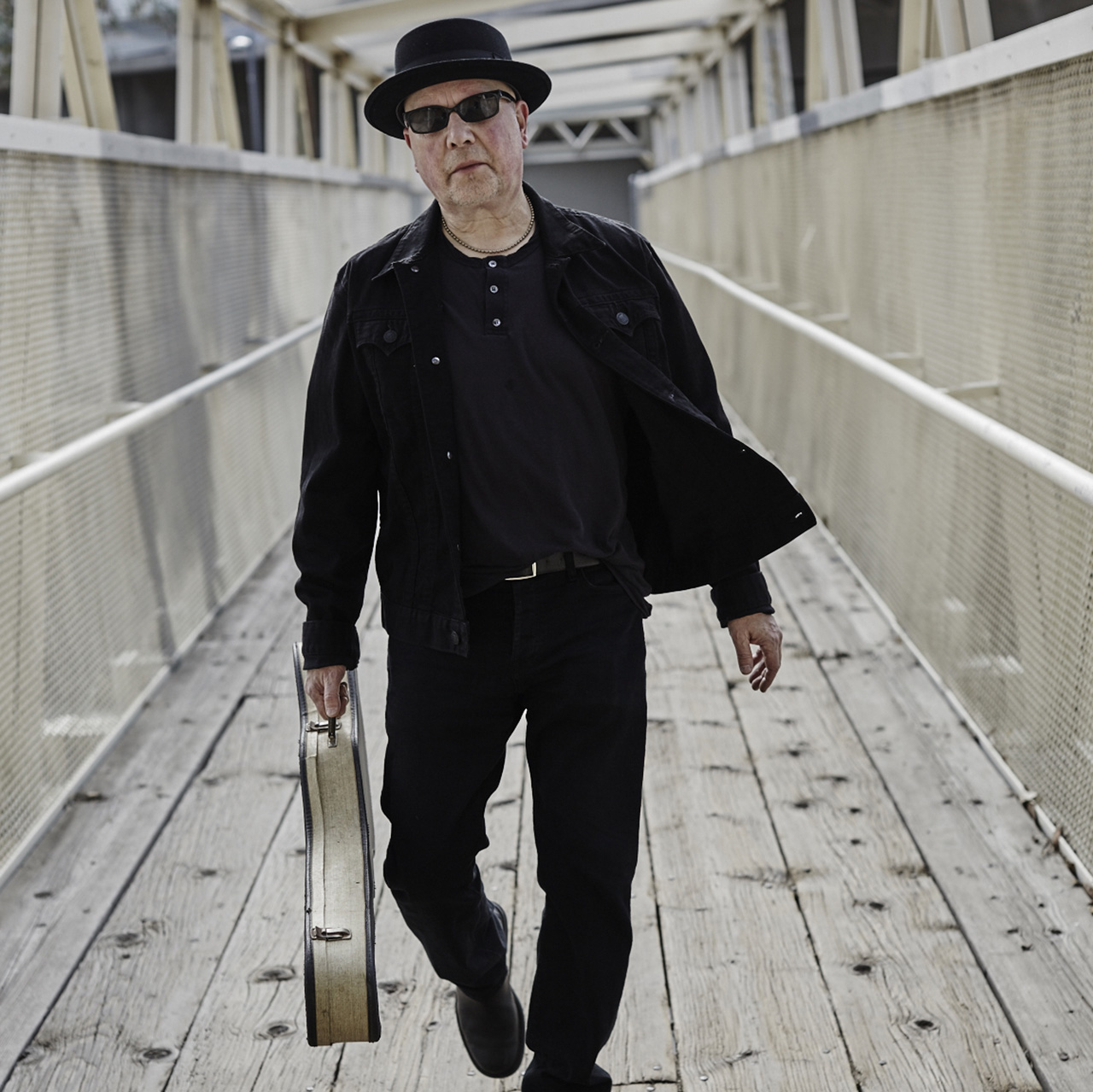 Corky James, pictured on a bridge, holding his guitar in its case