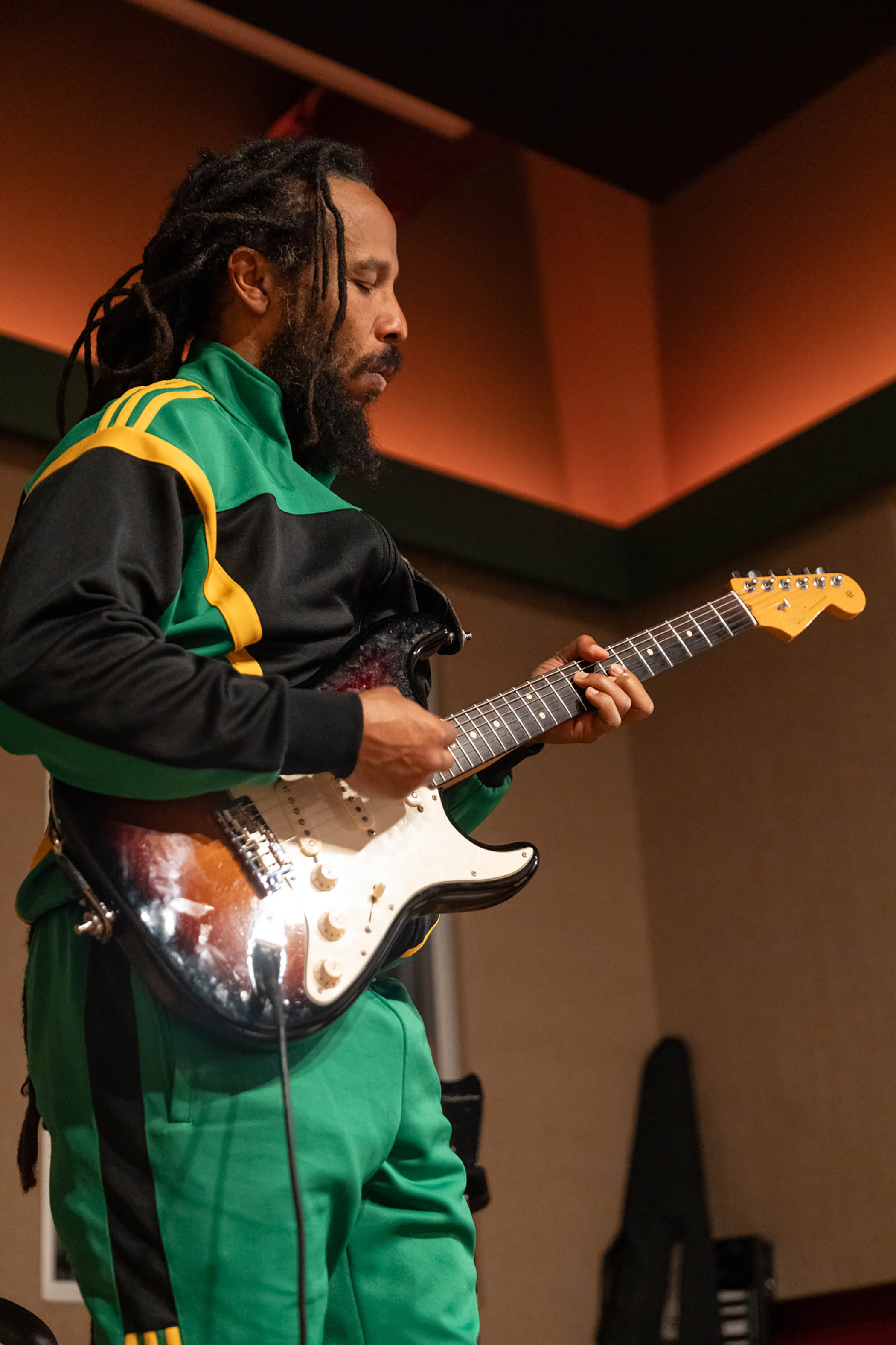Ziggy Marley wears a Jamaican flag tracksuit and plays his Fender Stratocaster
