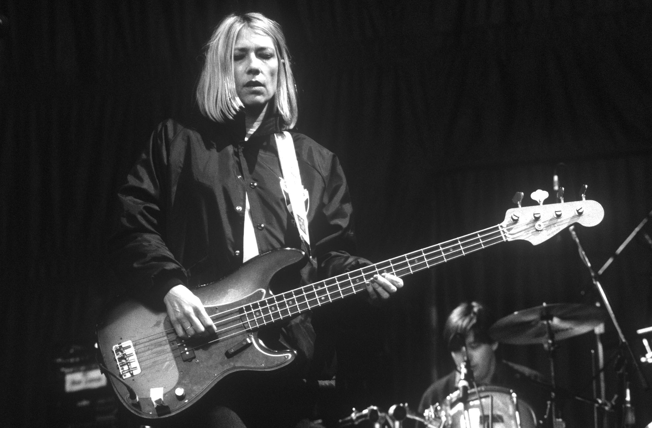 A black-and-white live shot of Kim Gordon playing live with Sonic Youth in 1995.