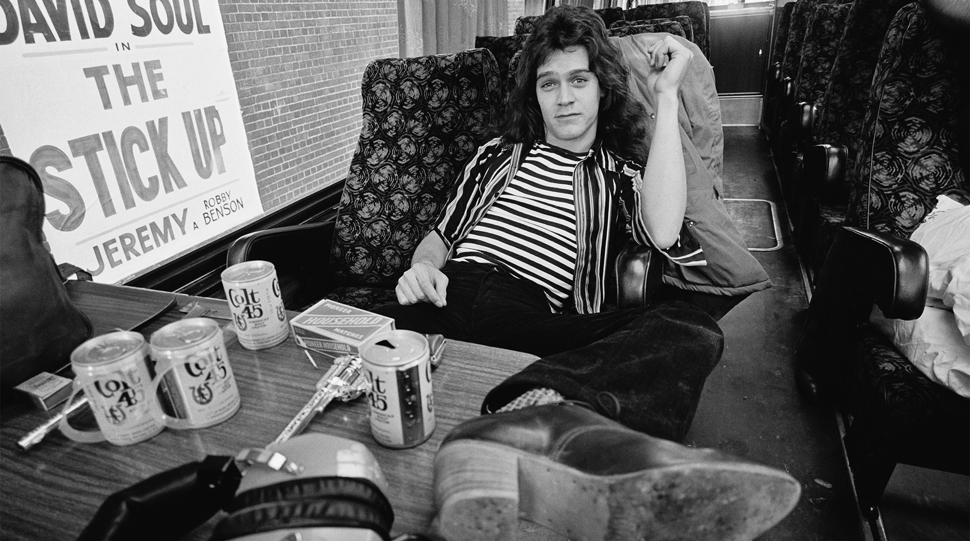Eddie Van Halen from Van Halen poses in their their tour bus outside Lewisham Odeon in London on 27th May 1978. On the table in front of him are various beer cans and a replica hand gun.