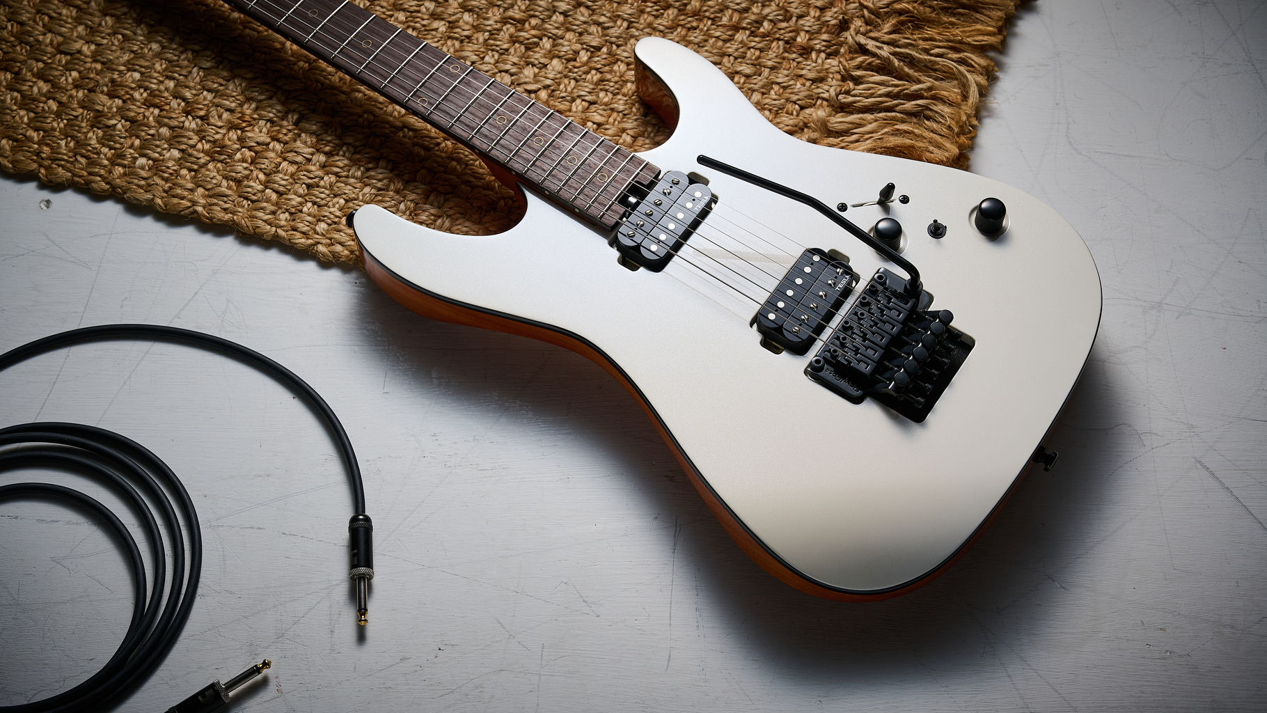 A Harley Benton Fusion IV HH electric guitar lying on a rug and white floor with a guitar cable nearby