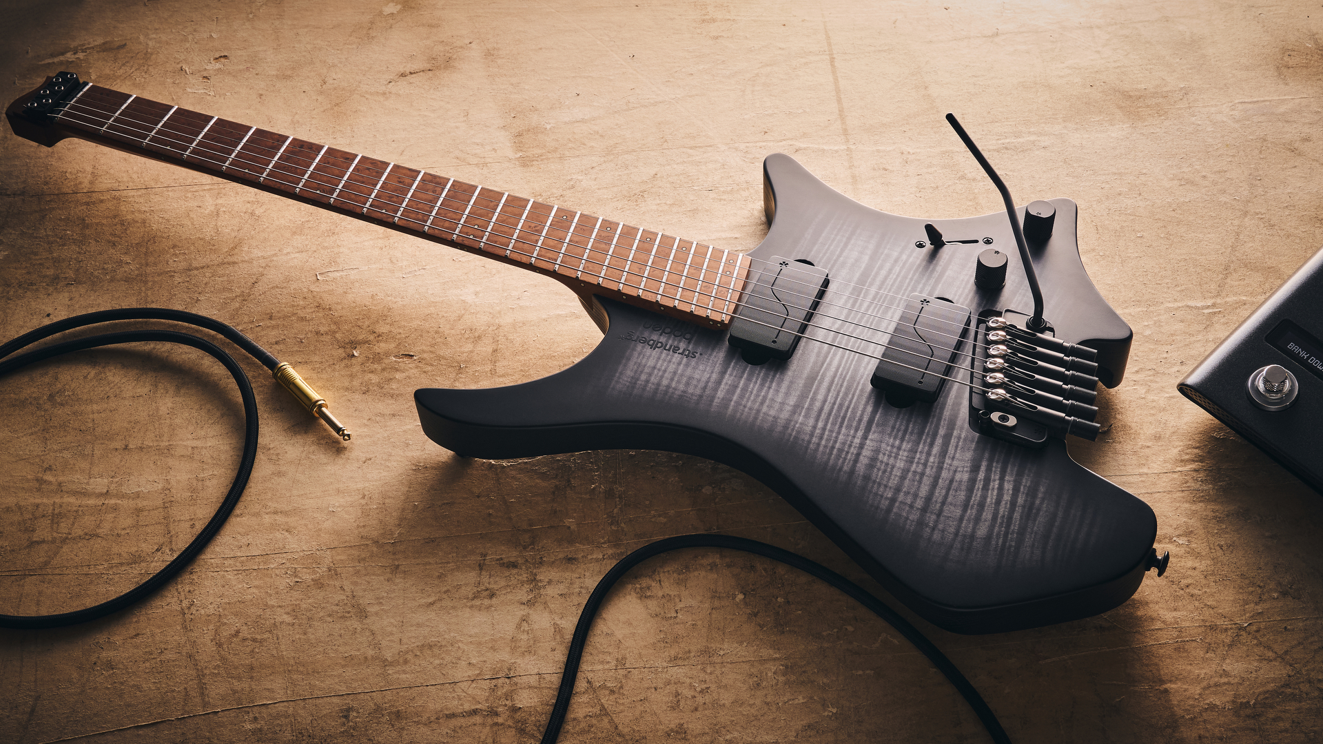 A Strandberg Boden Original N2.6T headless electric guitar lying on the floor with a guitar cable trailing nearby