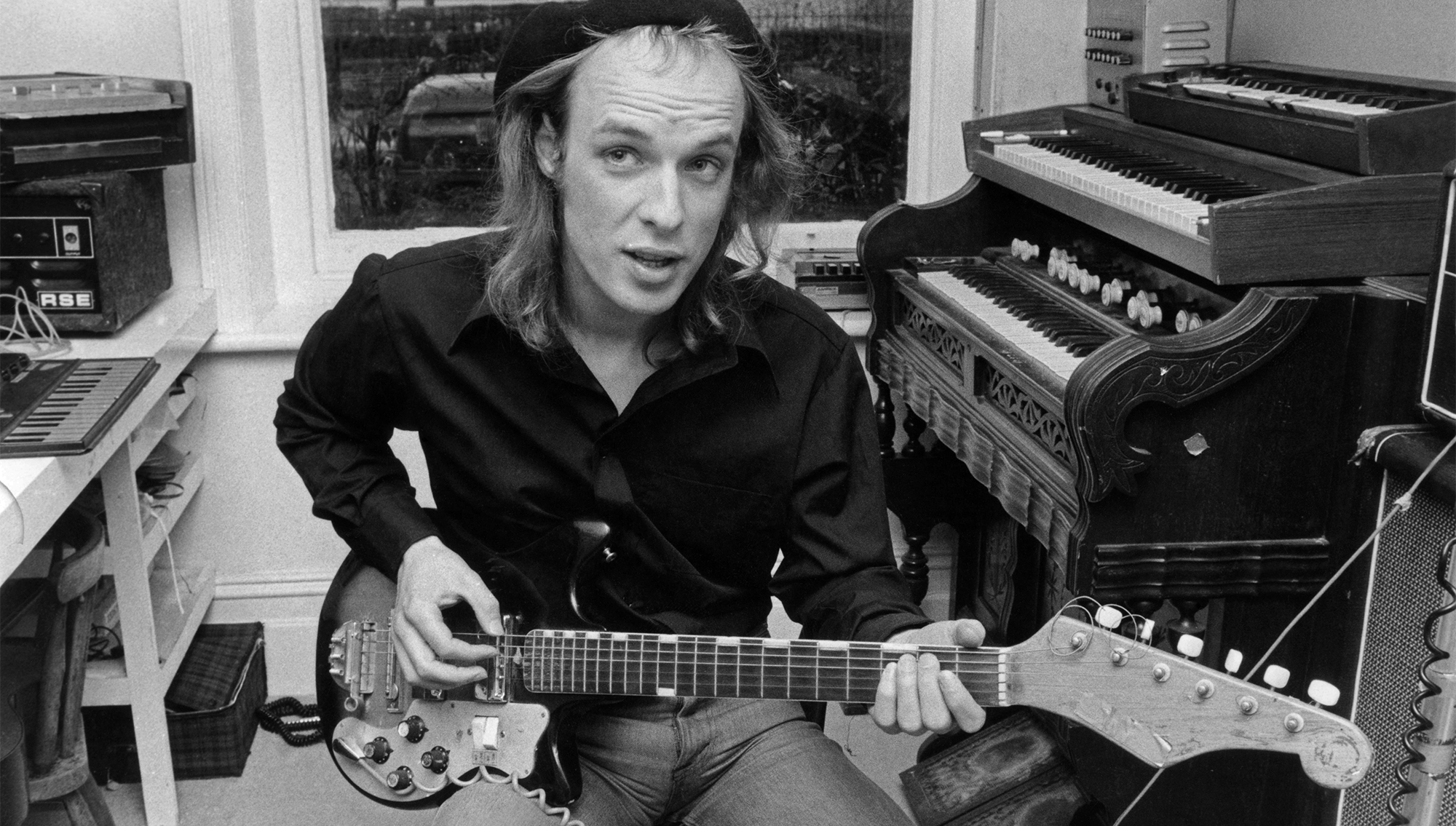Brian Eno at home playing an electric guitar in December 1974